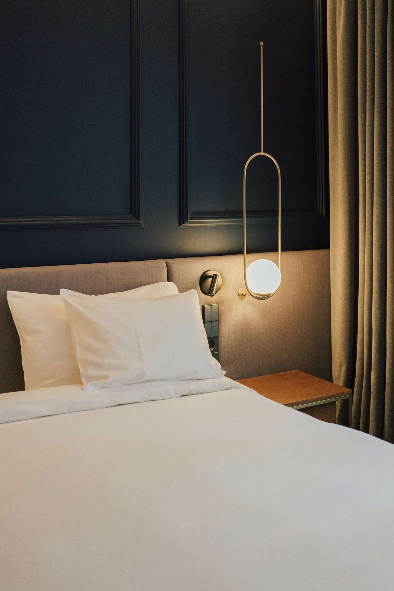 Hotel bedroom with navy panelled wall and brass pendant